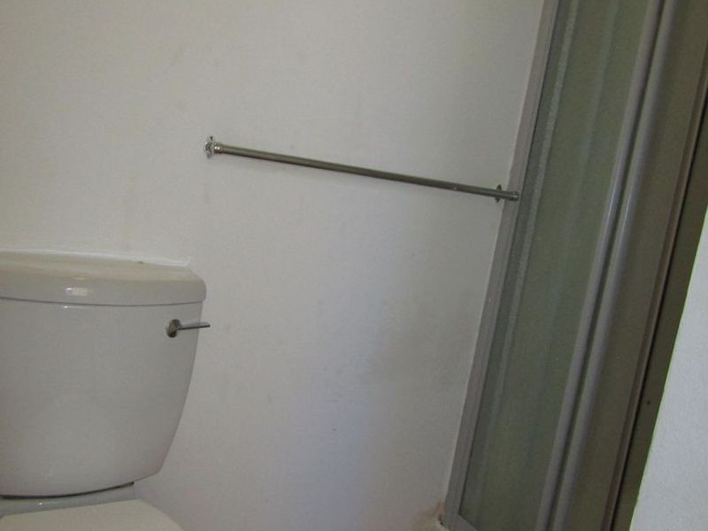 A compact bathroom featuring a toilet, shower enclosure, and laminate flooring, requiring some cosmetic attention to the base of the shower unit.