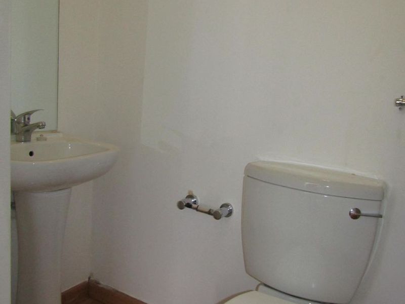 A compact bathroom featuring a white pedestal basin, a standard toilet, and laminate flooring, providing a functional and clean space.