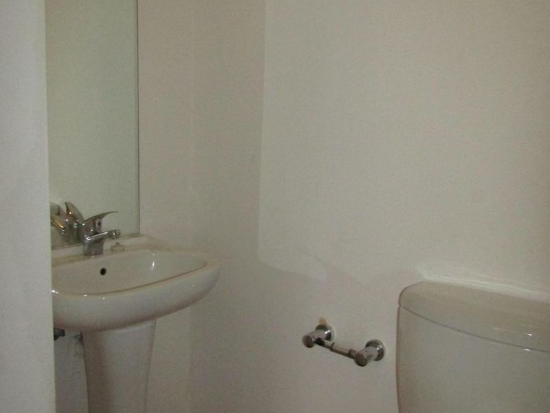 A compact bathroom featuring a pedestal basin, chrome mixer tap, wall-mounted mirror, and a standard toilet with laminate flooring.