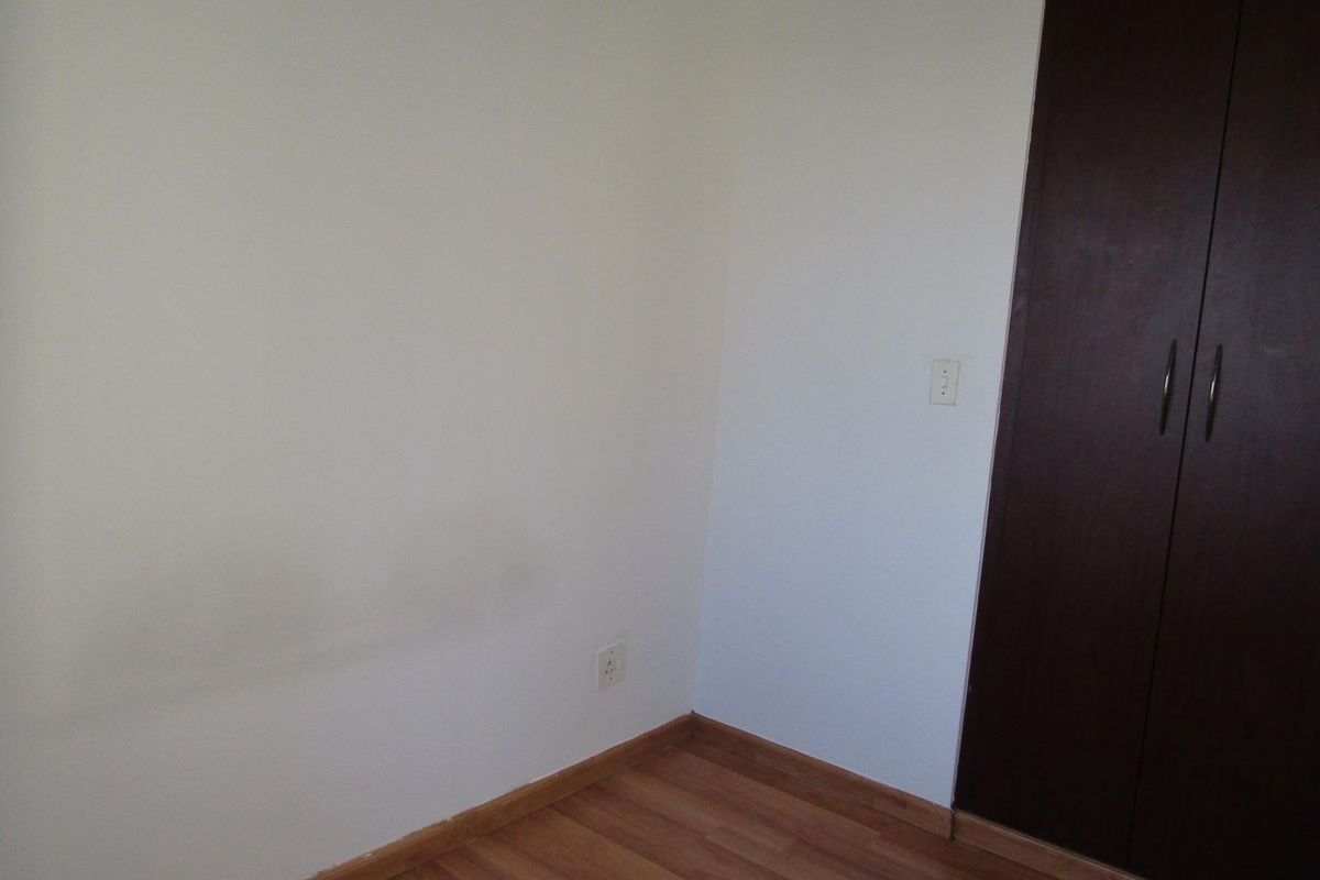 An empty bedroom featuring laminate flooring and a built-in dark wood wardrobe, requiring minor cosmetic wall repairs.