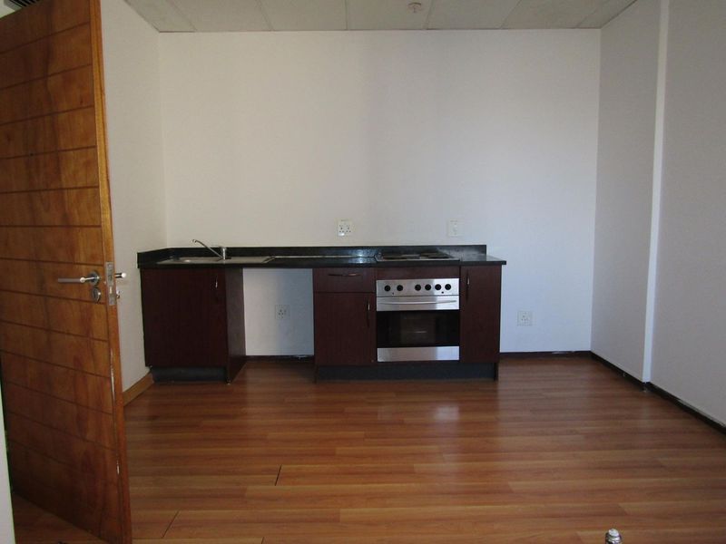 A compact, empty kitchen area featuring dark wood cabinetry, a built-in oven with hob, and laminate flooring, ready for a modern update.