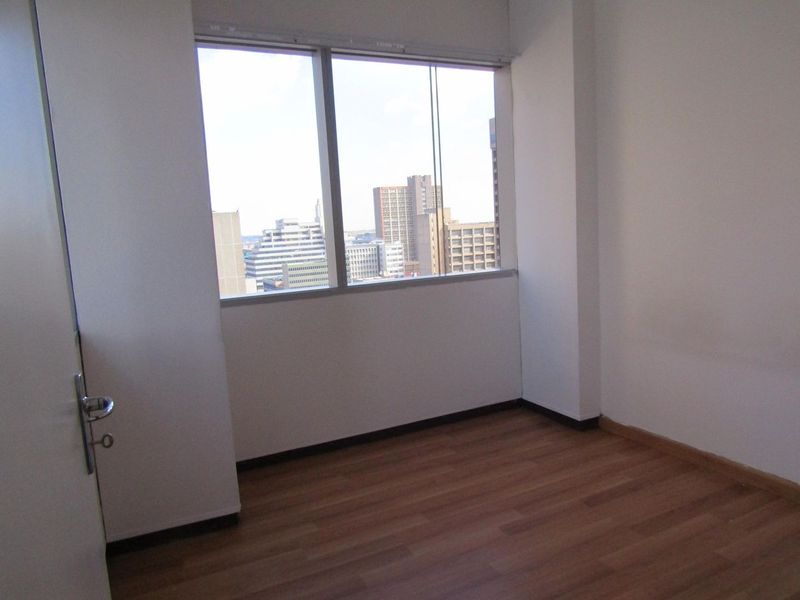 An empty bedroom featuring laminate flooring and a large window with an urban city view.