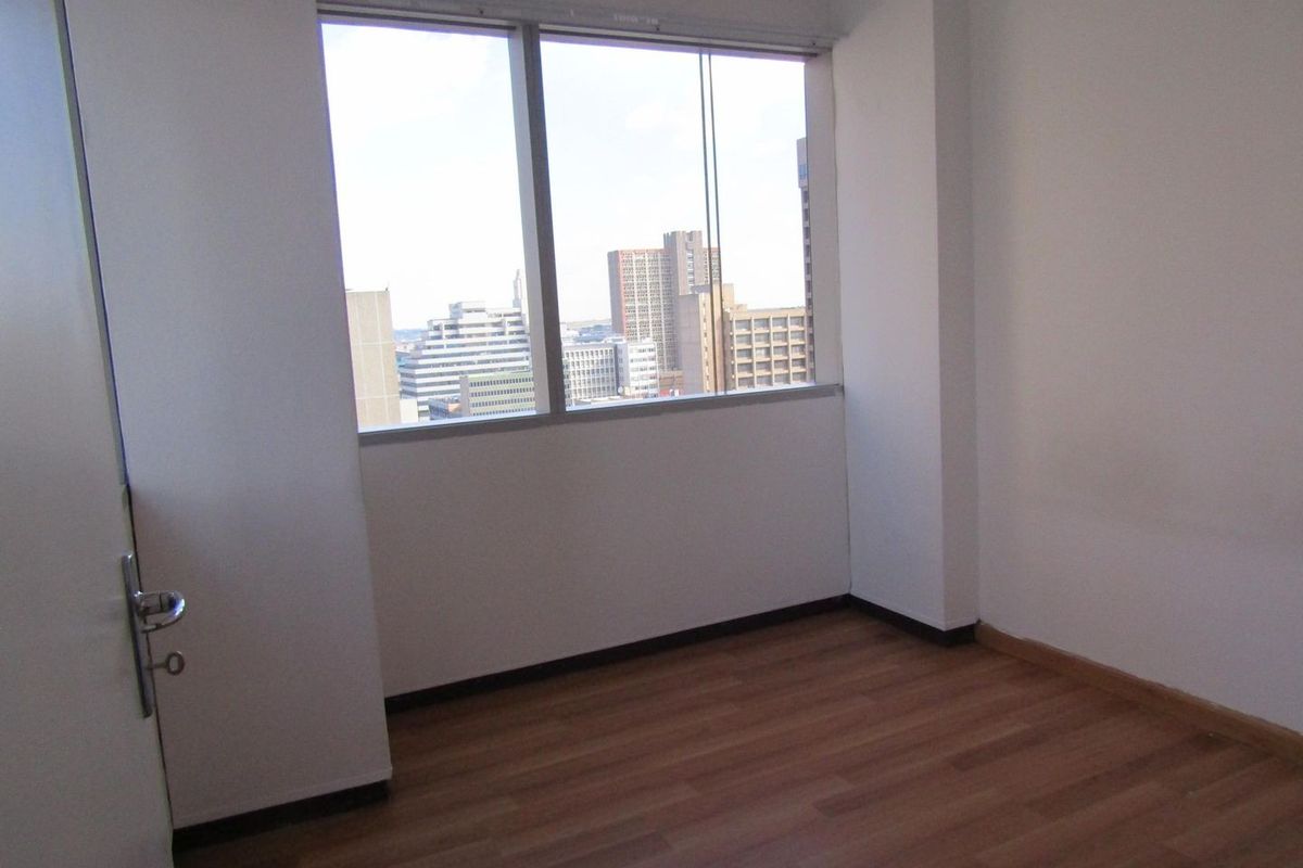 An empty bedroom featuring laminate flooring and a large window with an urban city view.