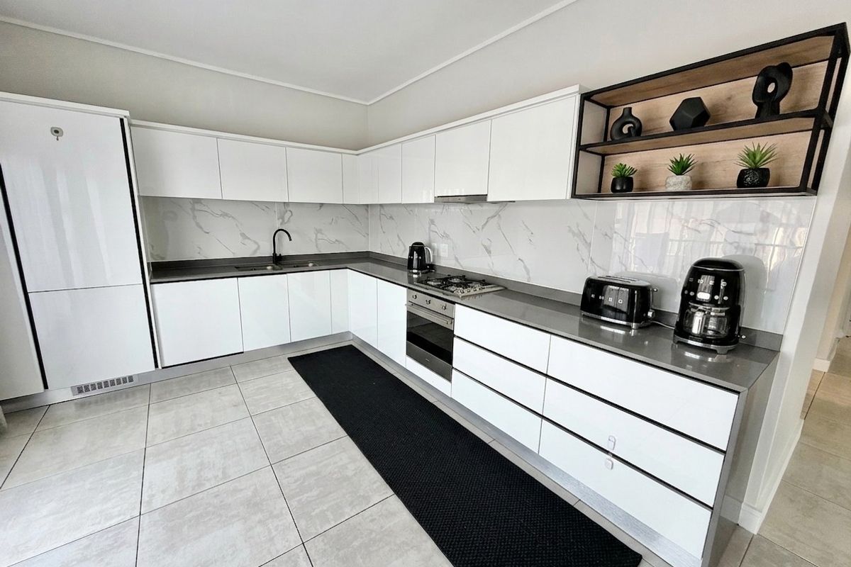 Modern kitchen featuring sleek white cabinetry, stone countertops, marble-look splashback, integrated oven, gas hob, and open shelving.