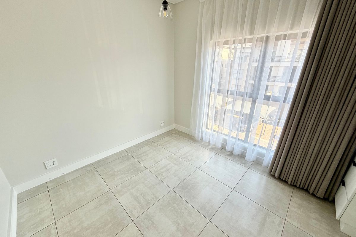 A bright, empty bedroom featuring modern large-format floor tiles, a large window with sheer curtains, and a minimalist pendant light fixture.