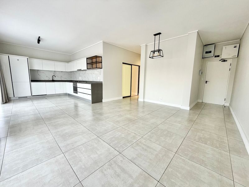 Spacious open-plan living area featuring a modern kitchen with sleek white cabinetry, stone countertops, integrated appliances, and large format floor tiles.