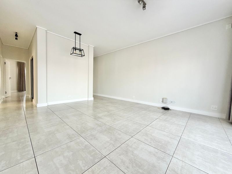 A bright, spacious, and empty living area featuring modern large-format floor tiles, neutral walls, and contemporary pendant lighting.