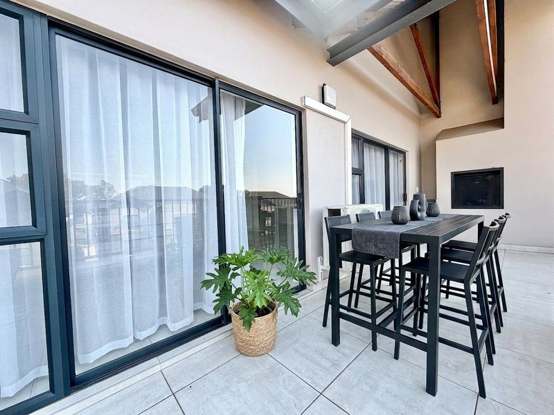 A spacious covered balcony featuring tiled flooring, exposed timber rafters, and a built-in braai, providing a seamless transition from the interior living space.