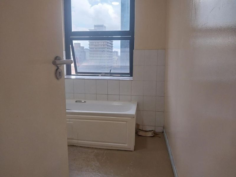 A compact bathroom featuring a built-in bathtub and tiled splashback, requiring cosmetic updates to the flooring and wall finishes.
