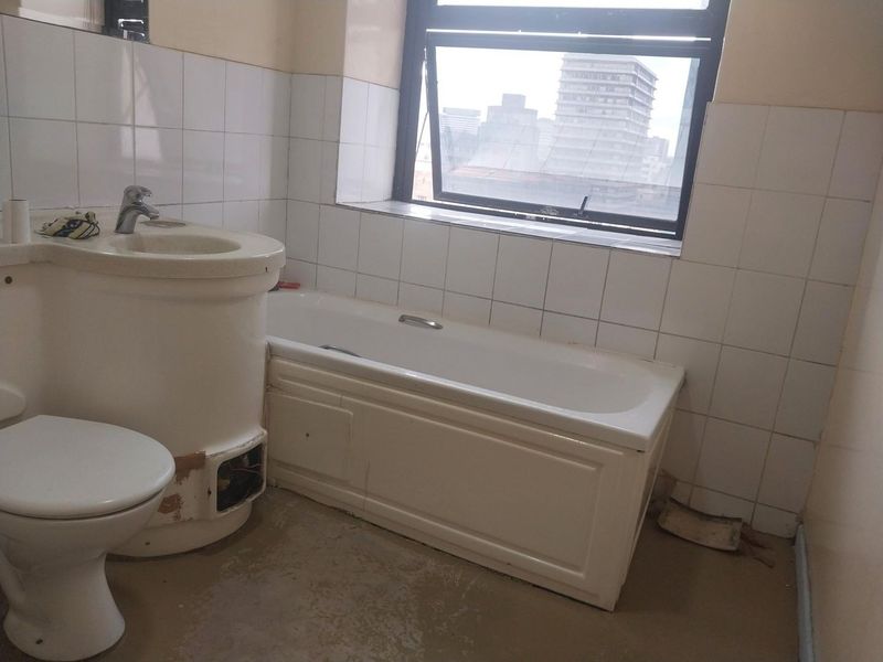 A dated bathroom featuring a bathtub, pedestal basin, and toilet, requiring significant renovation and new floor finishes to restore functionality and aesthetic appeal.