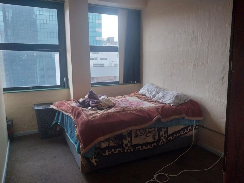 A bedroom featuring large windows with city views and exposed electrical conduit, requiring cosmetic updates to the walls and flooring.