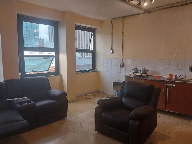 Open-plan living and kitchen area featuring basic cabinetry, tiled splashback, and large windows with urban views.