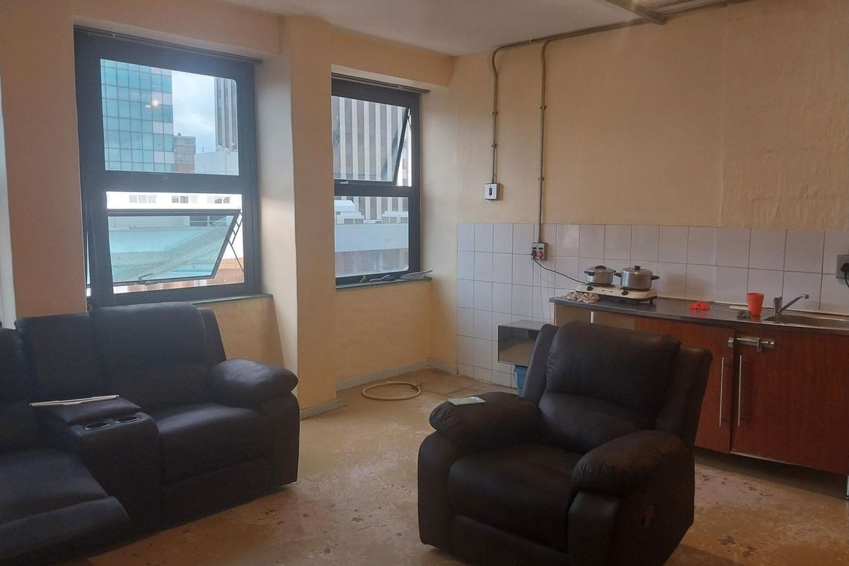 Open-plan living and kitchen area featuring basic cabinetry, tiled splashback, and large windows with urban views.