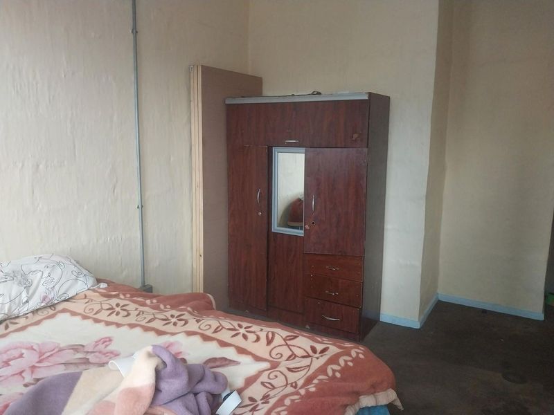 A bedroom featuring plain walls with exposed electrical conduit and basic flooring, requiring cosmetic updates to improve the overall aesthetic.
