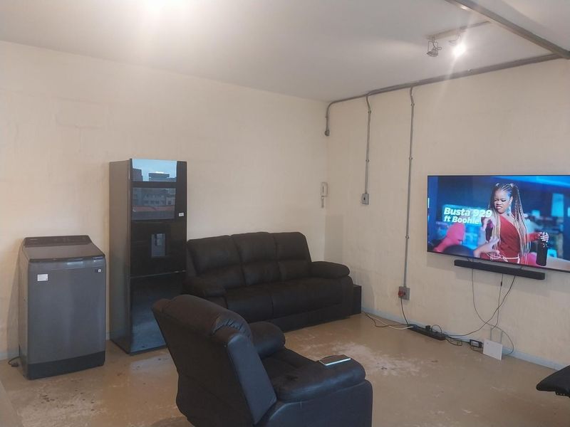 A living area featuring exposed electrical conduit, wall-mounted power points, and concrete flooring, offering a functional space with potential for cosmetic updates.