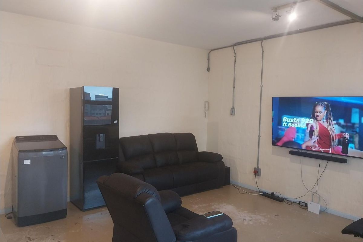 A living area featuring exposed electrical conduit, wall-mounted power points, and concrete flooring, offering a functional space with potential for cosmetic updates.