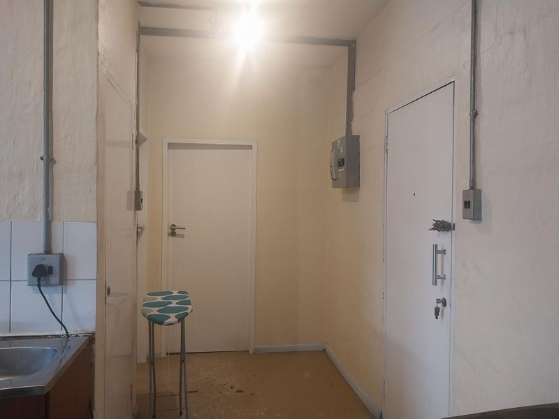 A functional hallway area featuring exposed electrical conduit, a distribution board, and a small sink area with tiled splashback.