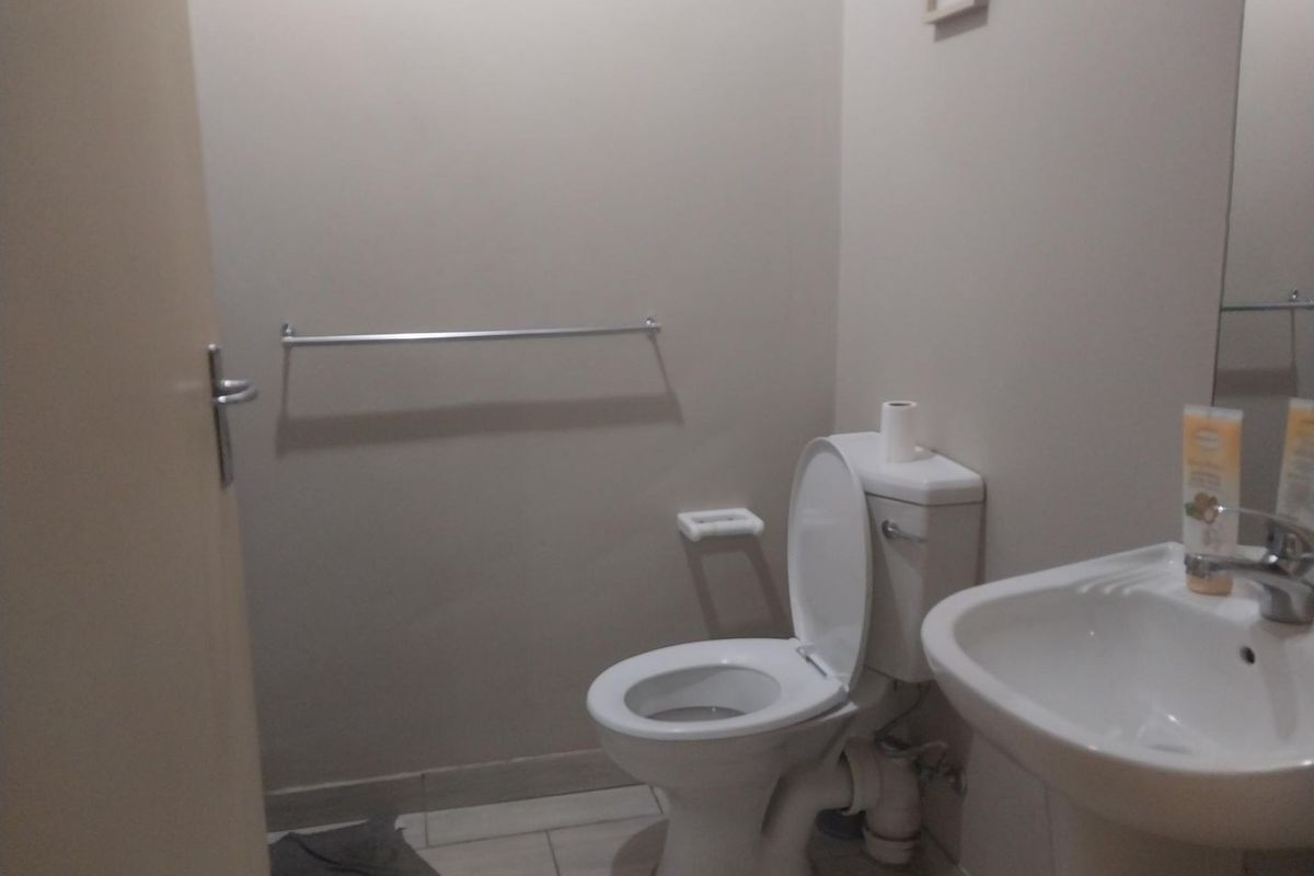 A functional bathroom featuring a standard toilet, pedestal basin, and wall-mounted towel rail with neutral wall finishes and tiled flooring.