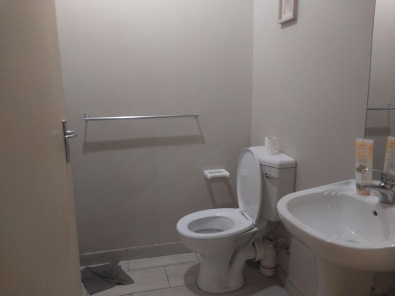 A functional bathroom featuring a standard toilet, pedestal basin, and wall-mounted towel rail with neutral wall finishes and tiled flooring.