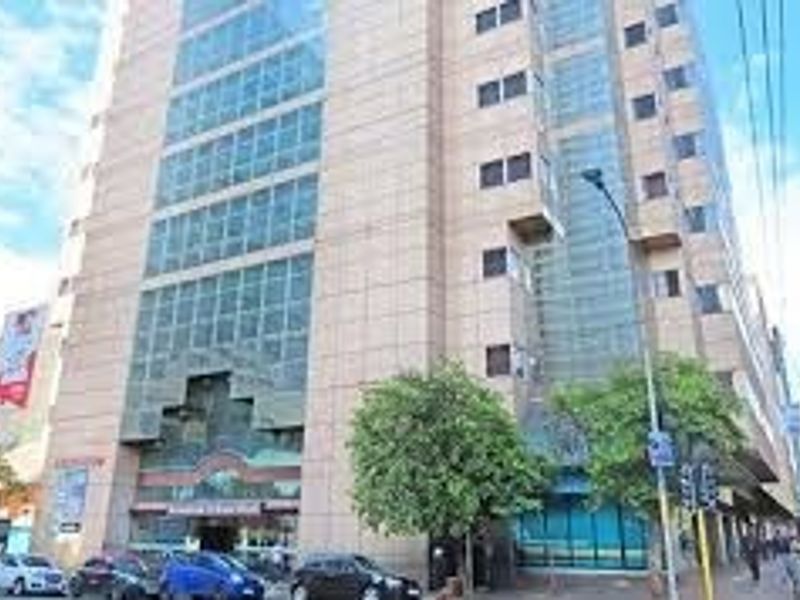 A multi-story apartment building facade featuring stone cladding and large glass window sections, situated on a busy street corner.