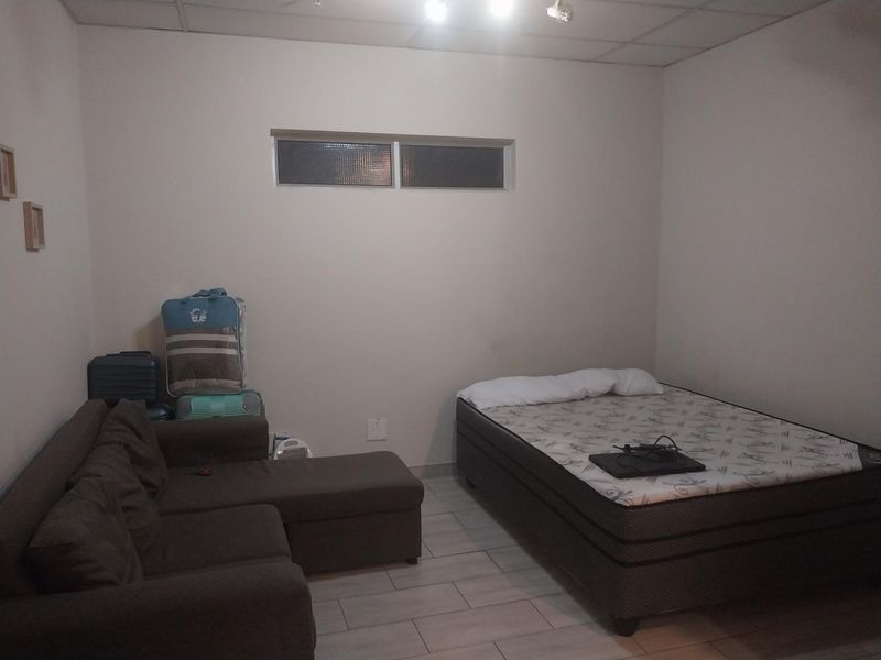A bedroom featuring tiled flooring, a drop ceiling, and a high-level window, providing a functional space for rest.
