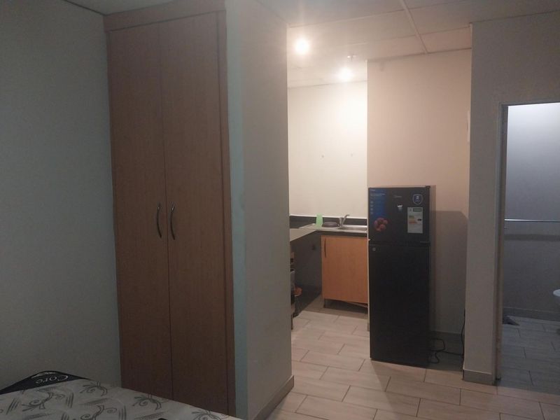 Open plan studio apartment featuring a kitchenette with sink, built-in wardrobe, and tiled flooring, with an adjacent bathroom entrance.