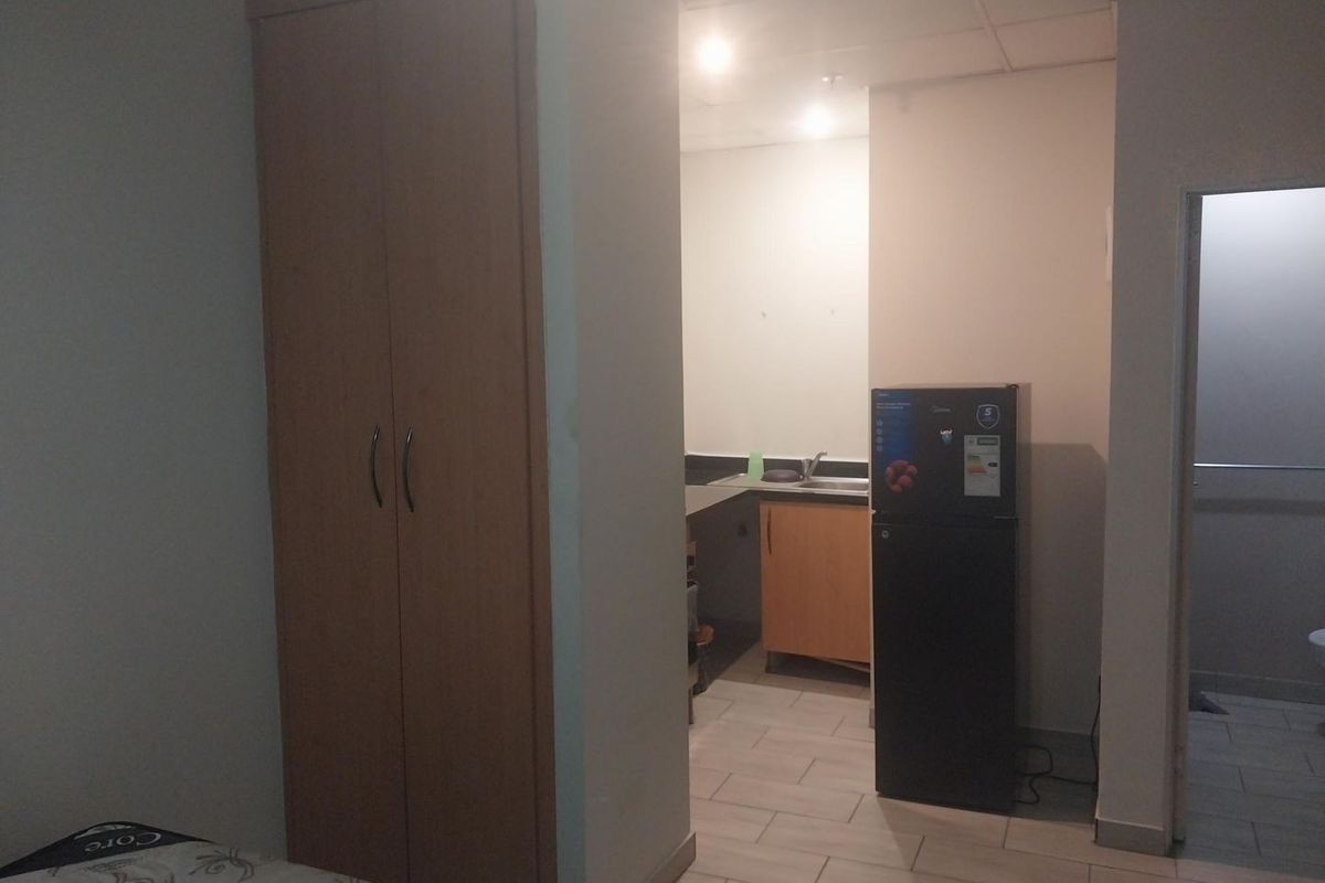 Open plan studio apartment featuring a kitchenette with sink, built-in wardrobe, and tiled flooring, with an adjacent bathroom entrance.