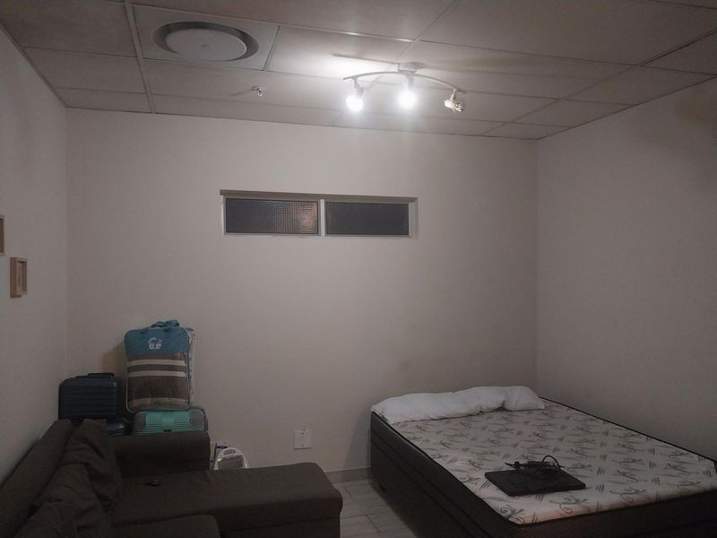 A bedroom featuring a suspended ceiling with recessed lighting and a high-set horizontal window, providing a functional space for rest.