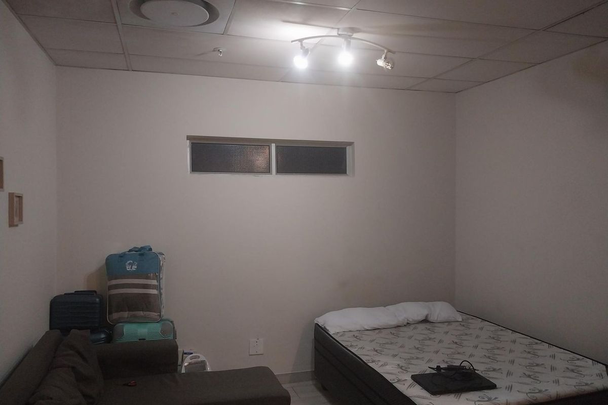 A bedroom featuring a suspended ceiling with recessed lighting and a high-set horizontal window, providing a functional space for rest.