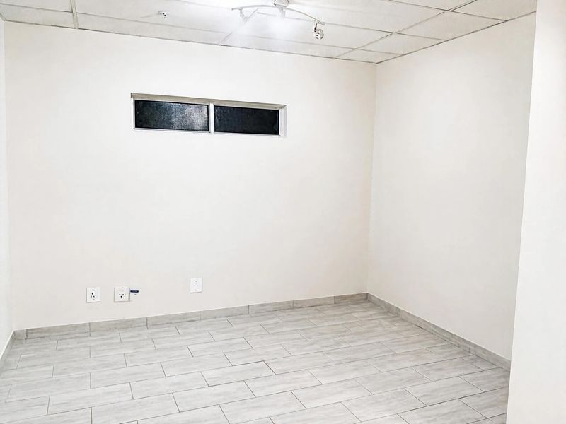 A clean, empty bedroom featuring neutral tiled flooring, a drop ceiling, and a horizontal window, providing a blank canvas for personalization.