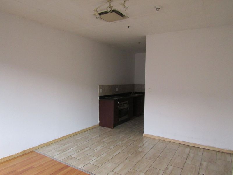 An empty open-plan living and kitchen area featuring tiled and laminate flooring, built-in cabinetry, and an integrated oven.