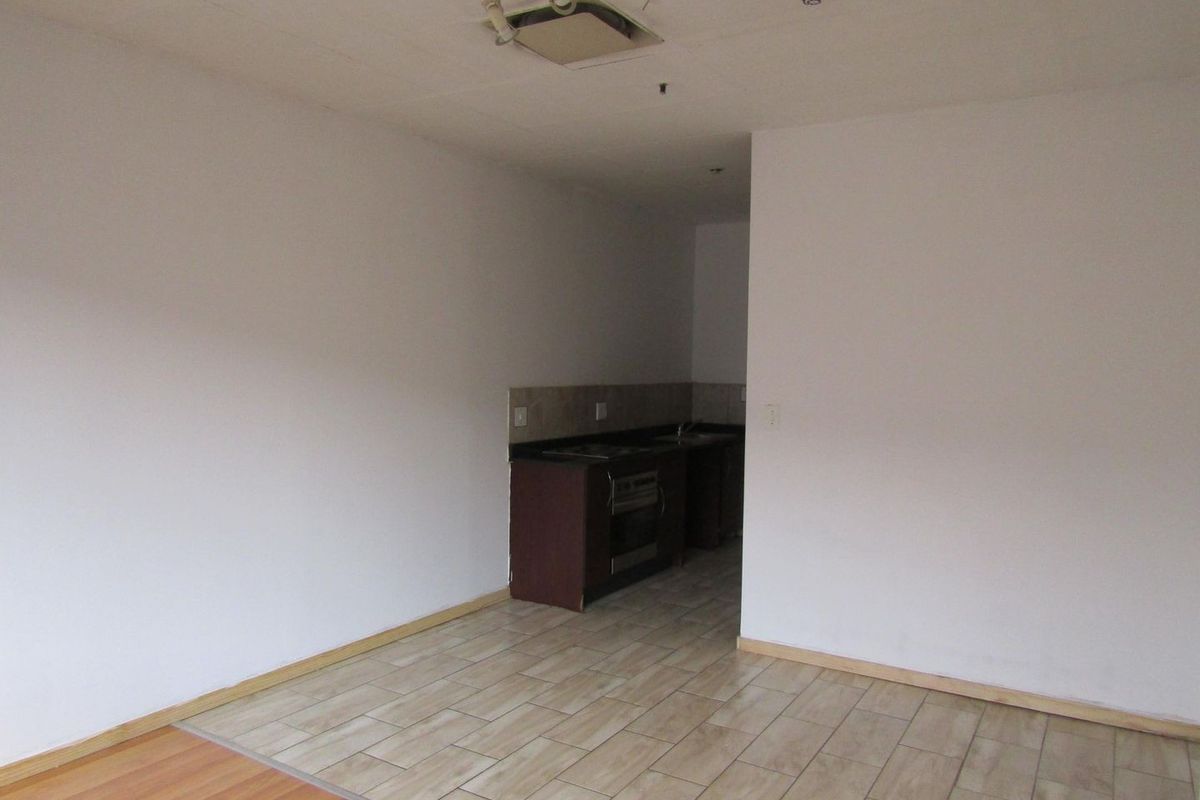 An empty open-plan living and kitchen area featuring tiled and laminate flooring, built-in cabinetry, and an integrated oven.