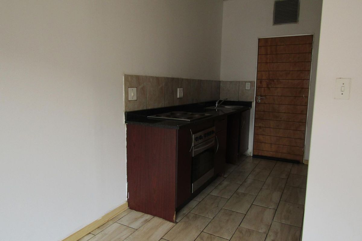 A compact, empty kitchen featuring dark cabinetry, stone countertops, a built-in oven, and tiled flooring, ready for a modern update.
