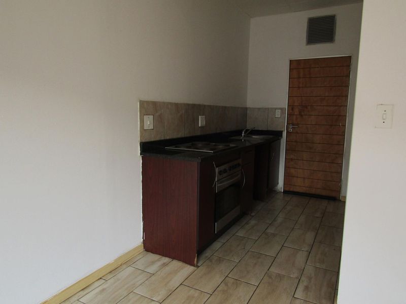A compact, empty kitchen featuring dark cabinetry, stone countertops, a built-in oven, and tiled flooring, ready for a modern update.