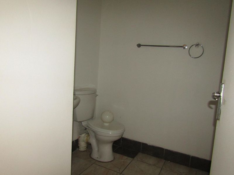 A compact bathroom featuring a standard toilet, towel rail, and tiled flooring, presenting a functional space in need of cosmetic updates.