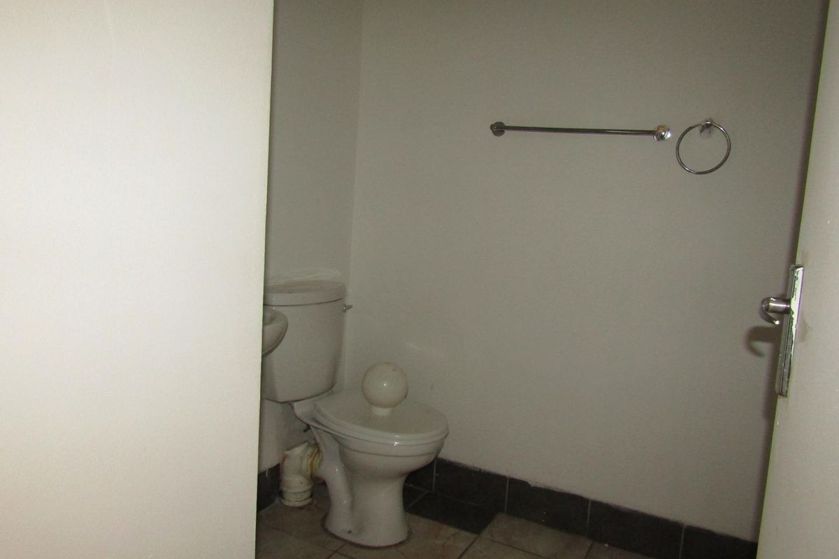 A compact bathroom featuring a standard toilet, towel rail, and tiled flooring, presenting a functional space in need of cosmetic updates.