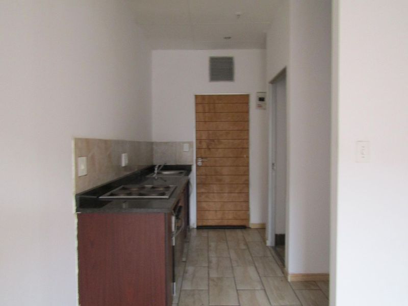 A compact kitchen area featuring granite countertops, an electric hob, built-in cabinetry, and tiled flooring in a clean, neutral space.