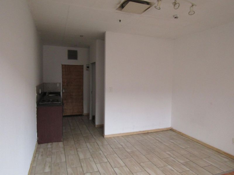 An empty open-plan living area featuring tiled flooring and a compact kitchenette with a built-in sink and hob.