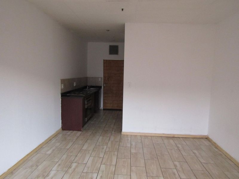 An empty open-plan living area featuring tiled flooring and a compact kitchen corner with built-in cabinetry, sink, and oven.