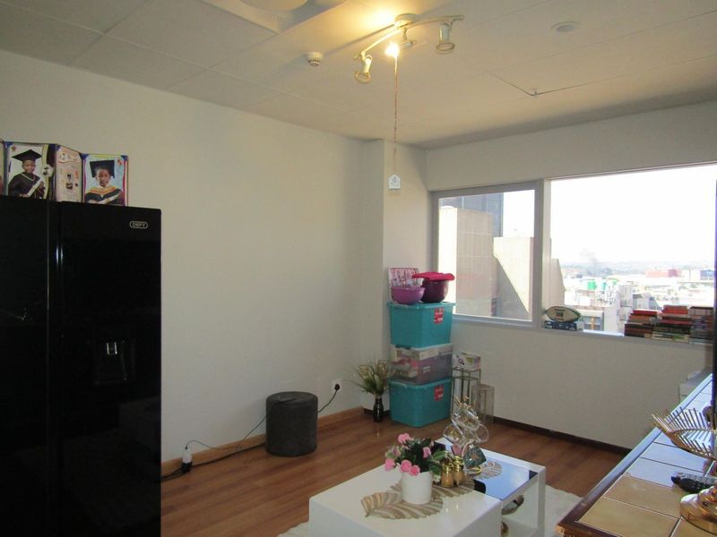 A living area featuring laminate flooring, a large window with urban views, and ceiling-mounted track lighting.