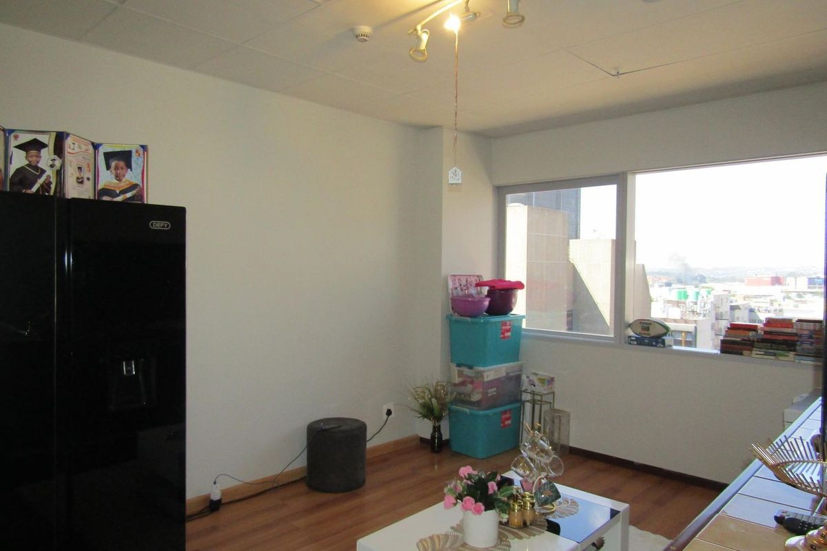 A living area featuring laminate flooring, a large window with urban views, and ceiling-mounted track lighting.