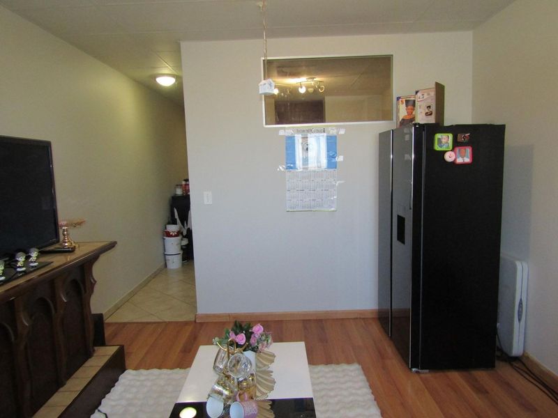 A living room area featuring laminate flooring, recessed lighting, and an internal window looking into an adjacent space.