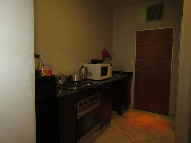 A compact kitchen featuring dark built-in cabinetry, granite countertops, and a built-in oven with hob, requiring improved lighting and cosmetic updates.
