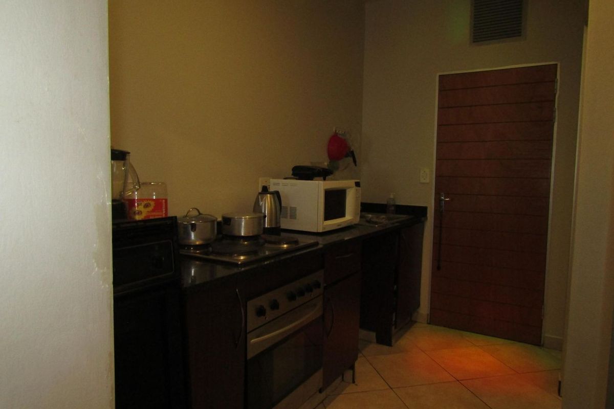 A compact kitchen featuring dark built-in cabinetry, granite countertops, and a built-in oven with hob, requiring improved lighting and cosmetic updates.