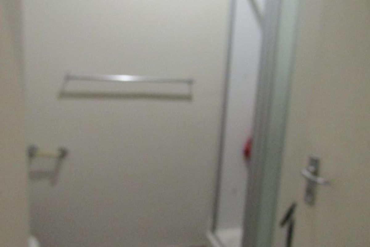 A compact bathroom featuring a shower enclosure, tiled flooring, and wall-mounted fixtures.