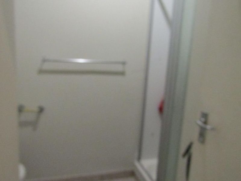 A compact bathroom featuring a shower enclosure, tiled flooring, and wall-mounted fixtures.