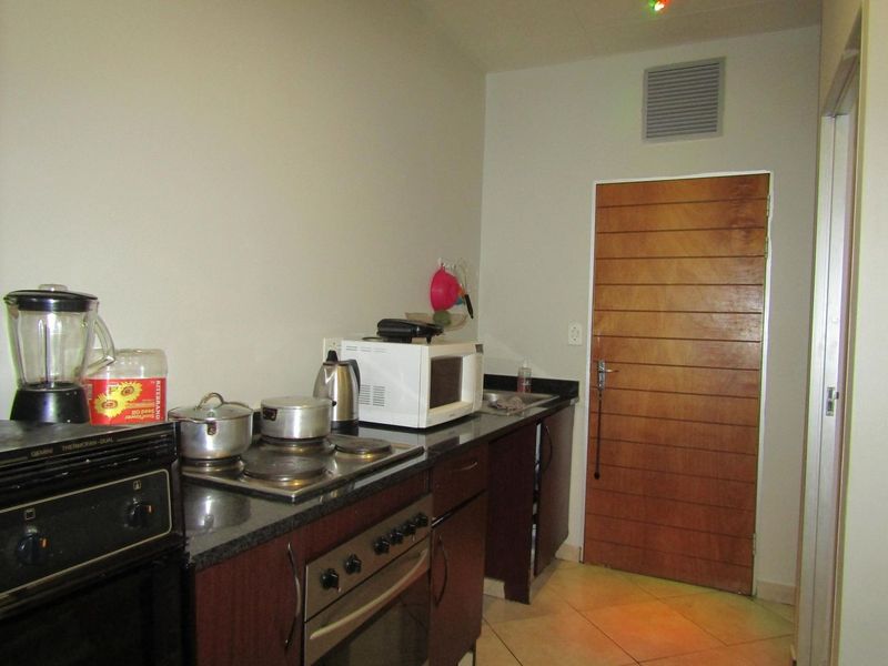 A functional kitchen featuring dark wood cabinetry, granite countertops, a built-in oven, and an electric hob, with tiled flooring and a wooden door.
