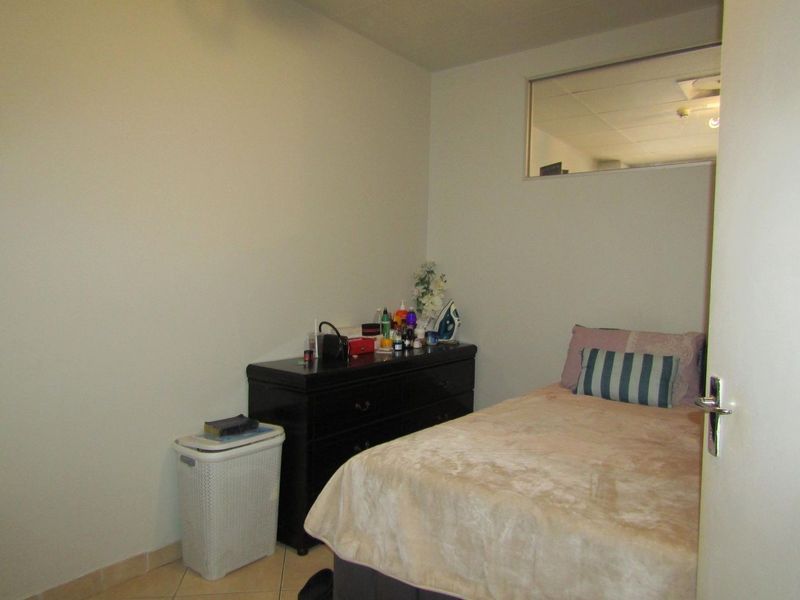 A compact bedroom featuring tiled flooring and a high-level transom window, providing a functional space with neutral wall finishes.