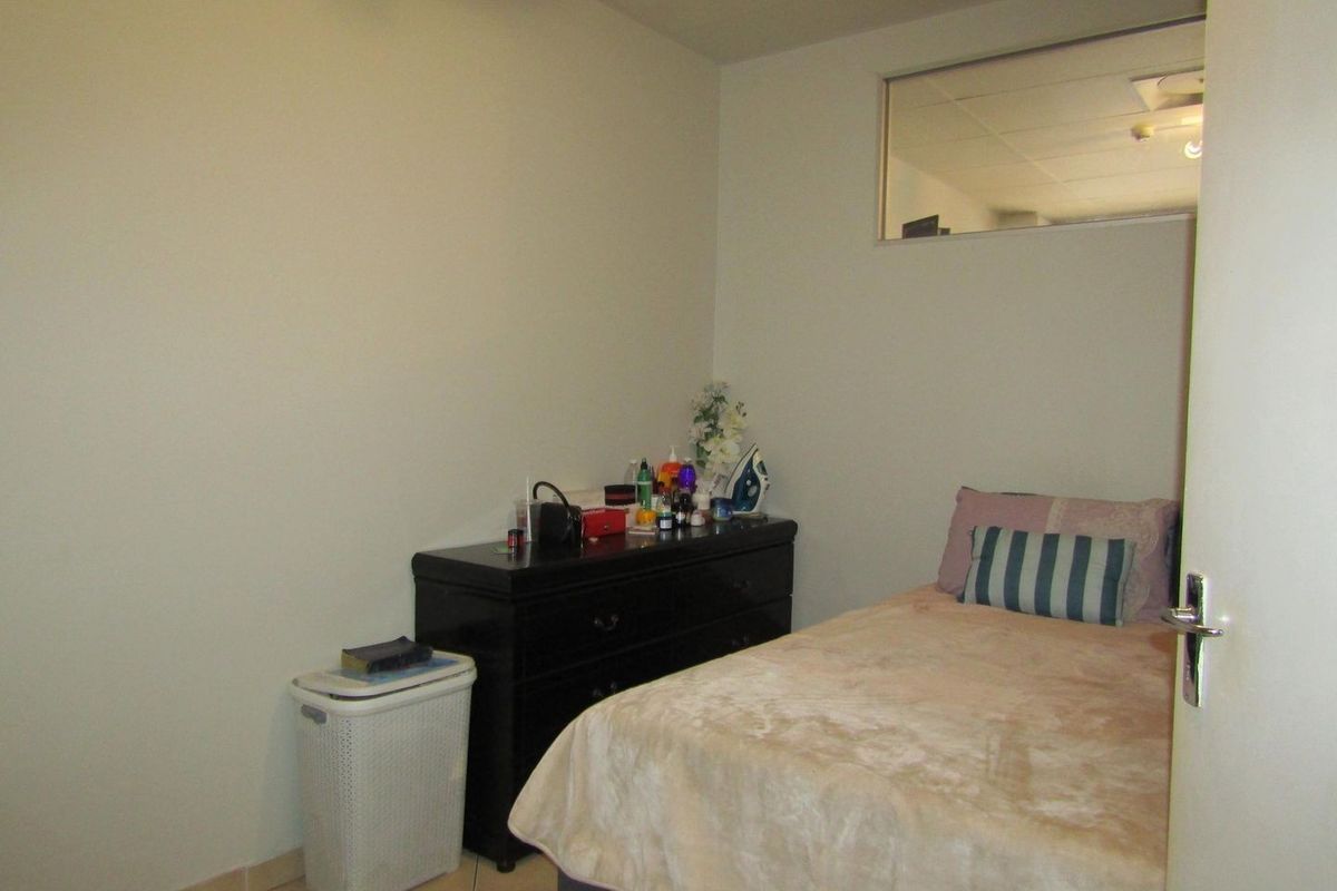 A compact bedroom featuring tiled flooring and a high-level transom window, providing a functional space with neutral wall finishes.