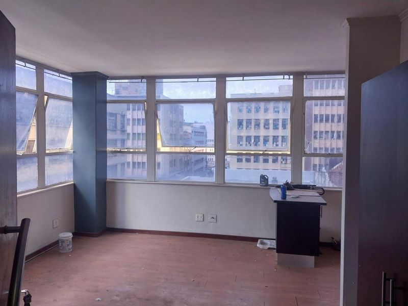 An empty living area featuring large windows with urban views, laminate flooring, and a neutral color palette, ready for renovation or staging.